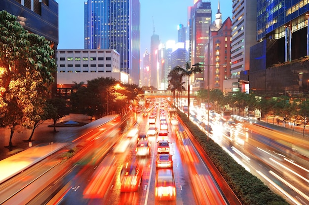 Rua de Hong Kong com tráfego movimentado e escritório de arranha-céus ao entardecer.
