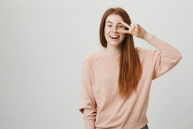 Ruiva amigável e otimista sorrindo e mostrando o símbolo da paz