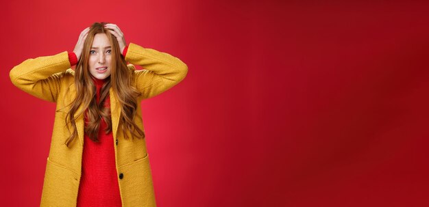 Foto grátis ruiva preocupada e assustada segurando as mãos na cabeça fazendo caretas preocupadas e preocupadas clenchin