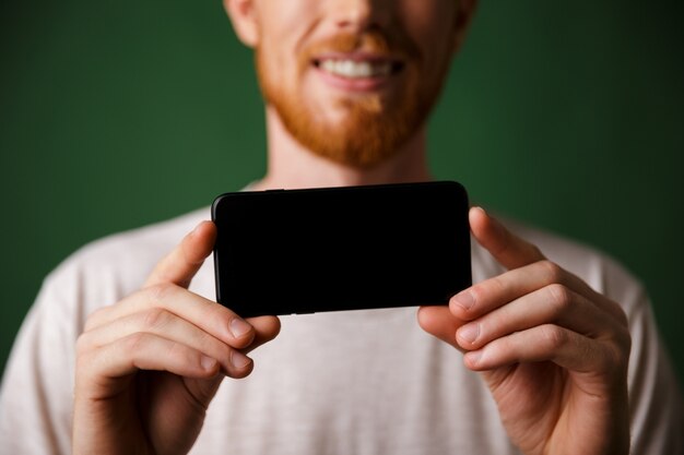 Ruivo de foto recortada homem barbudo em camiseta branca faz uma foto no smartphone móvel