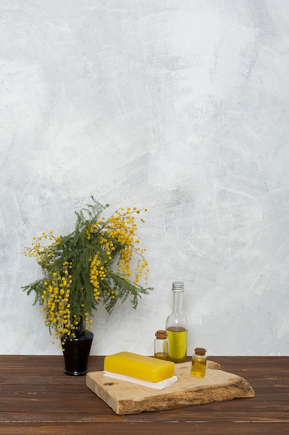 Foto grátis sabão de ervas amarelo no guardanapo dobrado e garrafa de óleo essencial perto do vaso de flor amarela mimosa