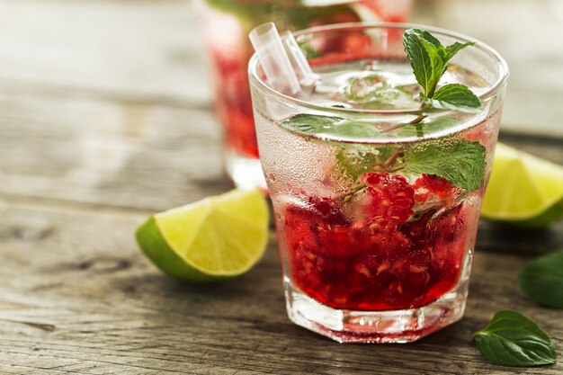 Sabão limonada de bebida fresca fria com framboesa, hortelã, gelo e lima em vidro em fundo de madeira. Fechar-se.