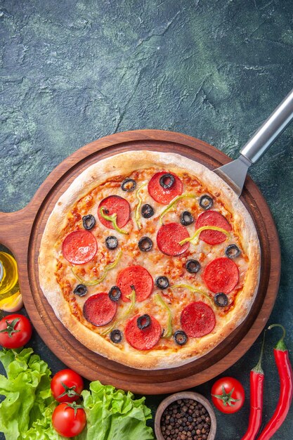 Saborosa pizza caseira em uma placa de madeira, garrafa de óleo, tomate pimenta verde pacote no fundo, em superfície escura