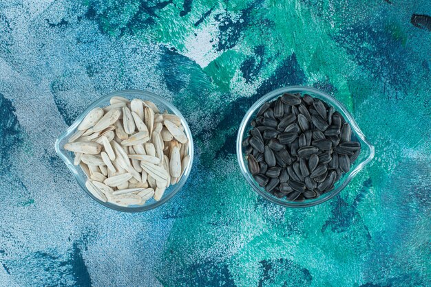 Saborosas sementes de girassol brancas e pretas em uma tigela de vidro, na mesa azul.