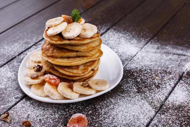 Saboroso café da manhã. Puncakes deliciosos com bananas, nozes e hortelã, servido na chapa branca