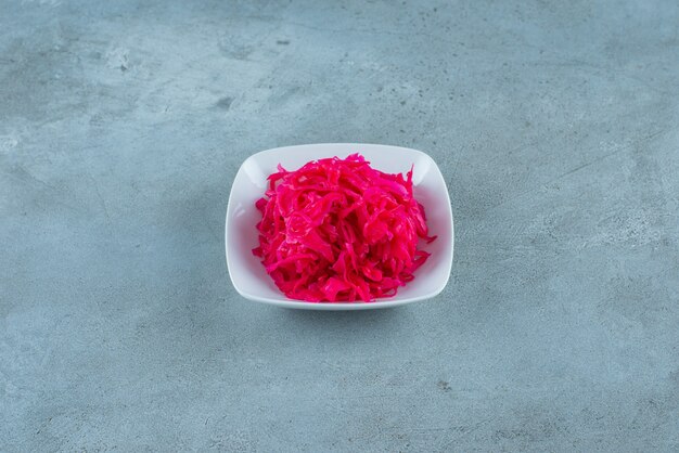 Saboroso chucrute vermelho picado fermentado em uma tigela, na mesa azul.