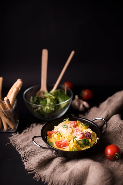 Saboroso macarrão espaguete cozido com folhas de manjericão e tomate no saco com varas de pão e salada veg