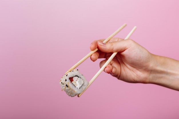 Saboroso sushi roll califórnia com pauzinhos de madeira no fundo rosa close-up. lugar para legenda e texto.