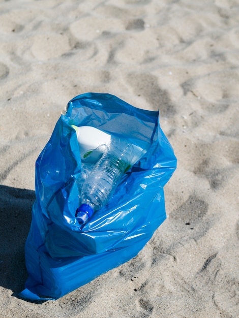 Saco azul de lixo de plástico na areia na praia