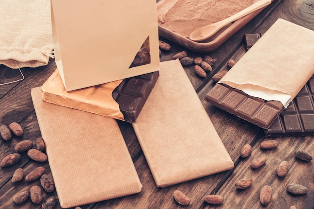 Saco de papel pequeno sobre a barra de chocolate embalada com grãos de cacau na mesa