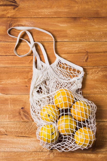 Saco reciclável com laranjas em fundo de madeira