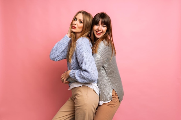 Saiu da mulher feliz na moda melhores amigos posando no fundo rosa no inverno, vestindo suéteres aconchegantes, dançando e comemorando, humor positivo.