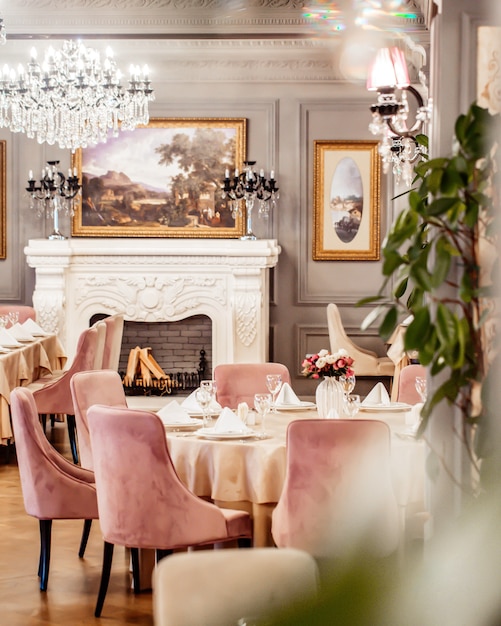 Sala de restaurante com mesa redonda algumas cadeiras lareira e plantas