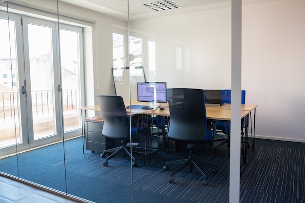 Sala de reuniões vazia atrás da parede de vidro. Sala de reuniões com mesa de conferência, mesa compartilhada para equipe e locais de trabalho. Gráficos de negociação no monitor. Interior de escritório ou conceito de imóveis comerciais