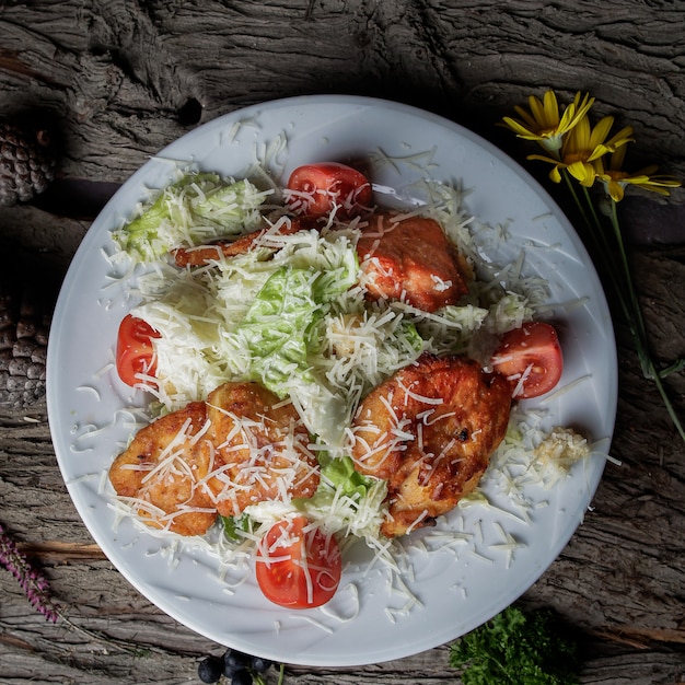 Salada caesar de close-up com frango, tomate, alface, azeitonas, biscoitos, queijo parmesão em um prato branco em uma casca de árvore escura