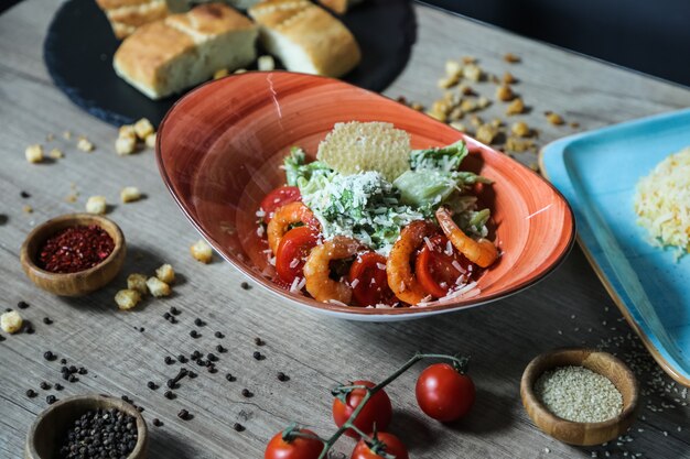 Salada caesar de vista lateral com camarões em um prato com tomates e speia