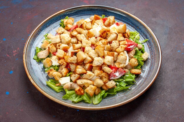 Salada César de vista frontal com vegetais fatiados e biscoitos em superfície escura