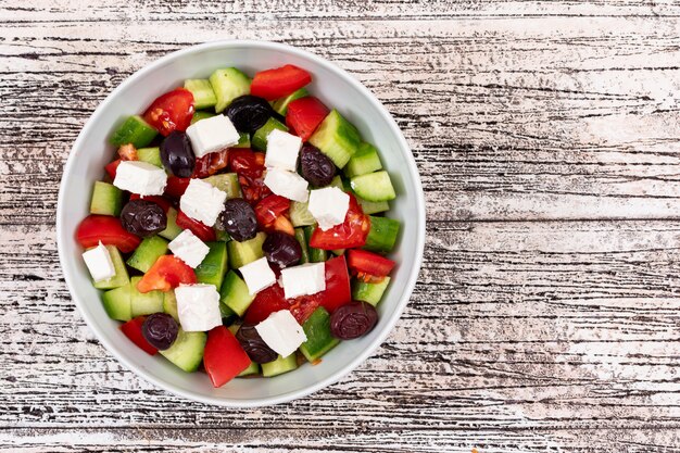 salada com queijo tomate pepino azeitona em uma tigela branca na mesa de madeira