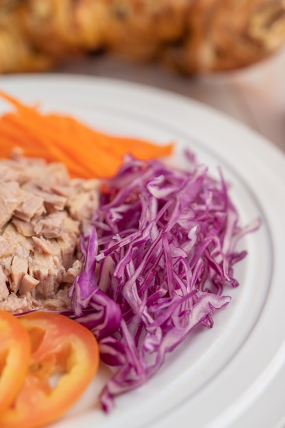 Salada de atum com cenoura, tomate, couve em um prato branco sobre um piso de madeira.