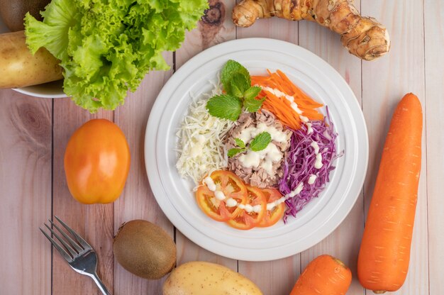 Foto grátis salada de atum com cenoura, tomate, couve em um prato branco sobre um piso de madeira.