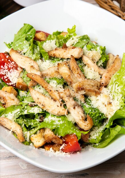 Salada de caesar do Parmesão da galinha com alface, os biscoitos do pão e os tomates de cereja frescos na placa branca.