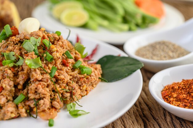 Salada de carne de porco picada picante em um prato branco com cebola roxa, capim-limão, alho, feijão, folhas de limão kaffir e cebolinha