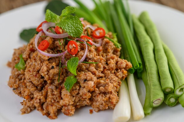 Salada de carne de porco picada picante em um prato branco com lentilhas, folhas de limão kaffir e cebolinhas.