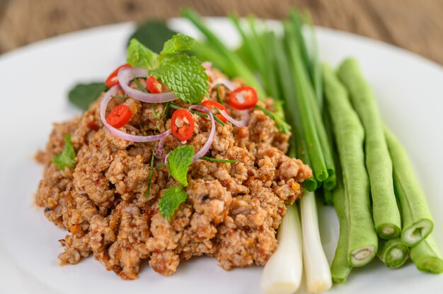 Salada de carne de porco picada picante em um prato branco com lentilhas, folhas de limão kaffir e cebolinhas.