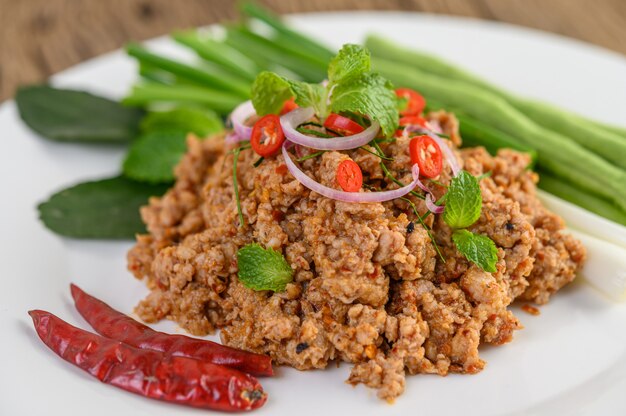 Salada de carne de porco picada picante em um prato branco com lentilhas, folhas de limão kaffir e cebolinhas.