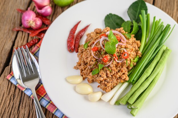 Salada de carne de porco picada picante em um prato branco com lentilhas, folhas de limão kaffir e cebolinhas.