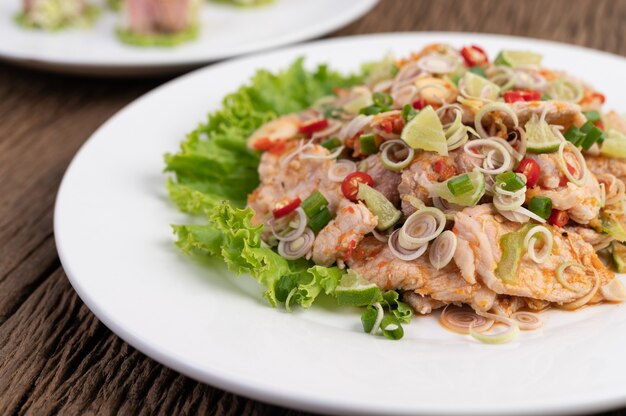 Salada de carne de porco picante com galangal, limão, pimenta, alho e coloque em uma salada em um prato branco.