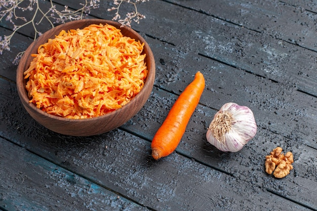 Salada de cenoura ralada de frente para dentro de um prato marrom na mesa rústica azul-escura salada de saúde dieta de cor de vegetais maduros