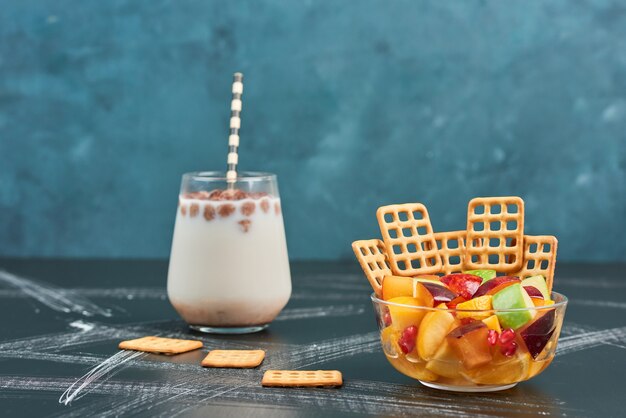 Salada de frutas com biscoitos e um copo de leite.