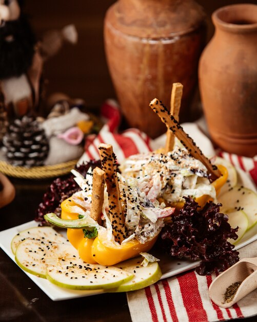 Salada de legumes de vista lateral com maionese em pimentão com fatias de maçã e sementes de gergelim