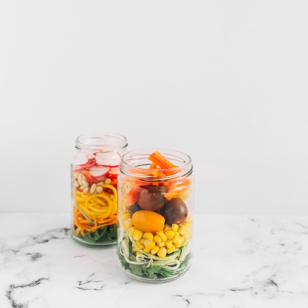 Salada de legumes em um frasco de pedreiro aberto na parte superior de mármore contra o fundo branco