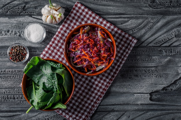 Salada de legumes em uma tigela com vista superior de verdes em um pano de piquenique e um fundo escuro de madeira.