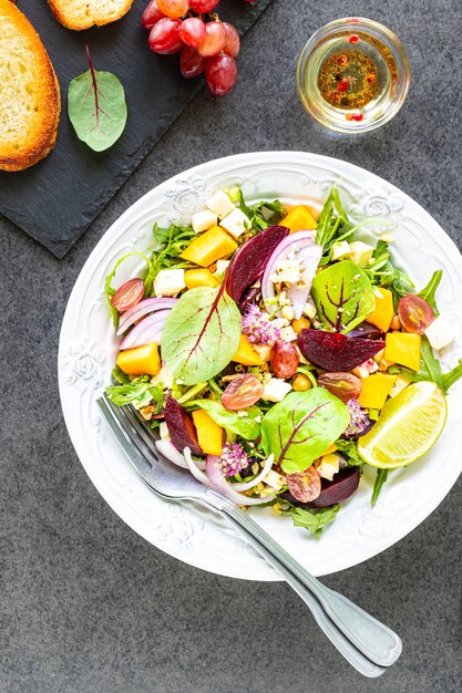 Salada de legumes fresca com beterraba, rúcula, cebola roxa e azeda em um prato branco com abóbora e uvas