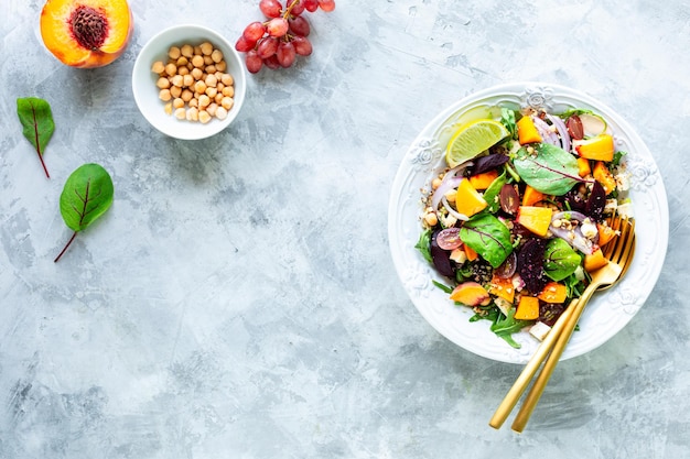 Salada de legumes fresca com beterraba, rúcula, cebola vermelha, azeda, grão-de-bico, pêssegos e uvas em um prato branco sobre um fundo de pedra branca Vista superior