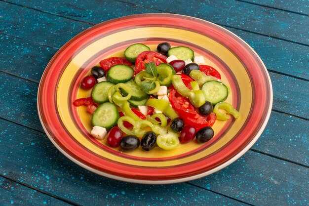 Salada de legumes fresca de vista frontal com pepinos fatiados, tomates, azeite e queijo branco dentro do prato com tomates na superfície azul-escura comida vegetal salada refeição lanche