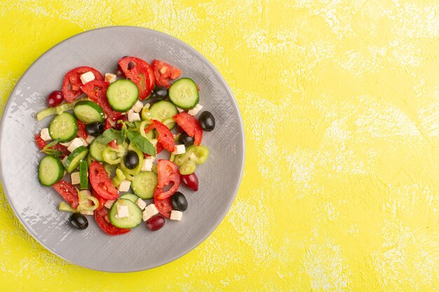 Salada de legumes fresca vista de cima com pepinos fatiados, tomates e azeitona dentro do prato na mesa amarela comida de vegetais salada refeição cor lanche