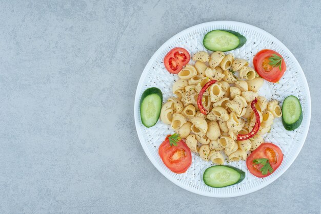 Salada de legumes no prato branco com delicioso macarrão no fundo de mármore