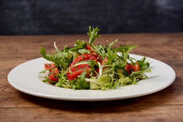 Salada de legumes no prato redondo branco na mesa de madeira.