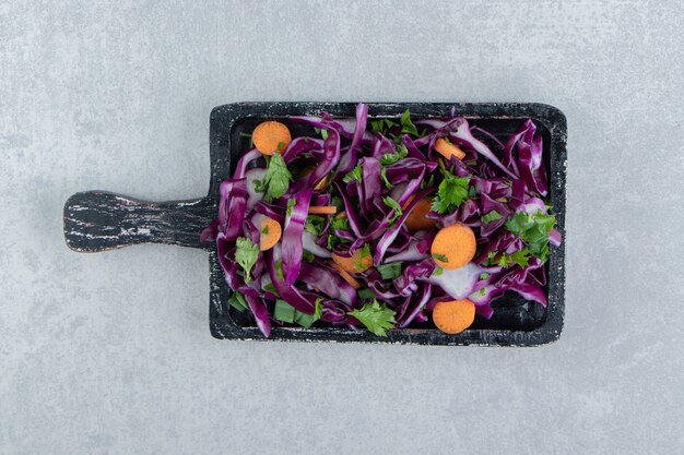 Salada de legumes picada na placa de madeira, no fundo de mármore.