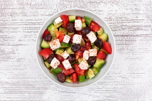 Salada de legumes queijo pepino tomate azeitona em uma tigela branca na superfície de madeira vista superior comida saudável