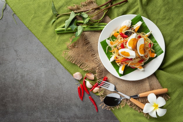 Salada de papaia servida com macarrão de arroz e salada de vegetais decorada com ingredientes da comida tailandesa.