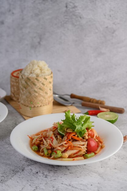 Salada de papaia tailandesa em um prato branco com arroz pegajoso