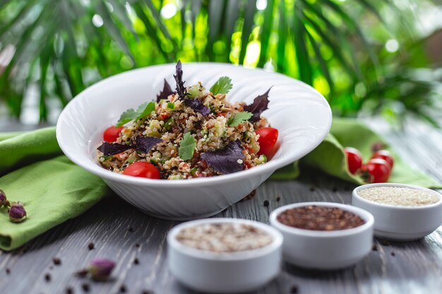 Salada de quinoa de vista lateral com pepino de tomate e sal de manjericão e pimenta em cima da mesa