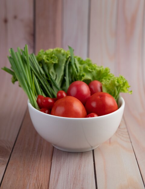 Salada de tomate e cebolinha em um copo branco sobre um piso de madeira.