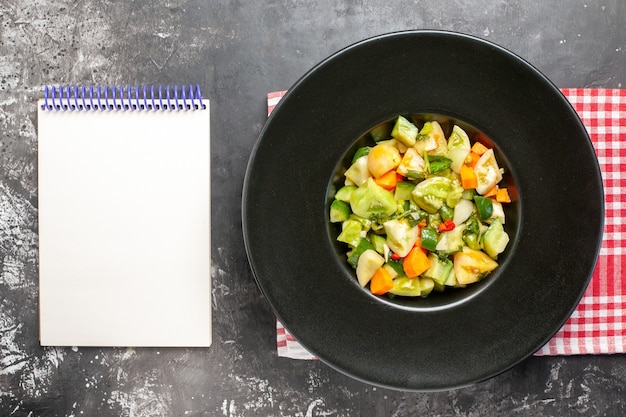 Salada de tomate verde vista de cima em bloco de notas de placa oval em fundo escuro