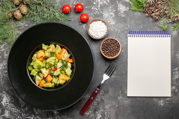 Salada de tomate verde vista de cima em prato oval um bloco de notas garfo especiarias em fundo escuro